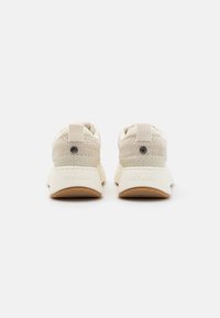 Cremefarvede sneakers med vævede stofoverdele, polstrede kraver og gummisåler med et struktureret design. Branding synlig på hælen.