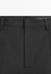 Pantalon noir sur mesure avec une ceinture fine, des passants pour ceinture et une fermeture avant dissimulée.
