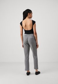 Svart bodysuit med lav rygg, parret med lysegrå tapered sweatpants. Outfiten har en glatt tekstur og subtile designdetaljer.