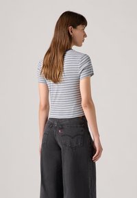 Gestreepte T-shirt met korte mouwen in blauw en wit, gecombineerd met hoge zwarte wijde jeans met een rood logo label op de achterkant.
