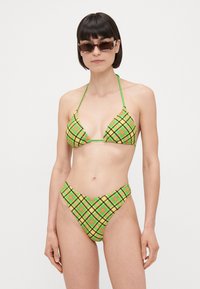 Grön rutigt bikini med triangelöverdel och högskuren underdel, med svarta och orange accenter. Justerbara band i nacken och ryggen.