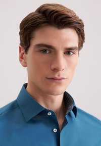 Cyan knoopoverhemd met een contrasterende gebosseleerde kraag, met een gladde textuur en een getailleerd ontwerp, benadrukt door witte knopen.