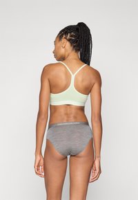 Sujetador deportivo verde claro con tirantes ajustables y un diseño sin costuras, combinado con braguitas grises que tienen una cinturilla con logo.