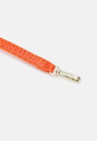 Sangle en simili cuir texturée orange avec un clip en métal doré, gravé "STEVE MADDEN," et un design tressé.