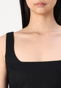 Top negru fără mâneci, cu decolteu pătrat, realizat dintr-un material texturat și ușor. Liniile netede și curate subliniază designul.