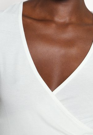 Close-up van de borst en nek van een persoon die een wit V-hals kledingstuk draagt, met gladde donkere huid en stoftextuur.