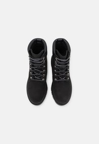 Botas de tobillo de ante negro con un cuello acolchado, cordones grises y ojales de metal, que cuentan con una suela de goma texturizada para mayor tracción.