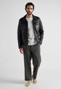 Zwarte leren jas met twee borstzakken, grijze trui, olijfgroene wijde broek en beige instapschoenen. Gladde textuur, gestructureerd ontwerp.