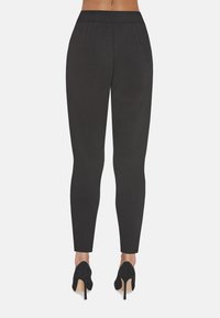 Czarne eleganckie spodnie o gładkiej fakturze, slim fit i średnim stanie, z przednimi zaszewkami i zwężanymi nogawkami, w połączeniu z czarnymi szpilkami.