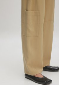 Khaki wijde broek met een zijzak, met een soepele textuur; gecombineerd met zwarte patenten ballerina's. Eenvoudig, casual ontwerp.