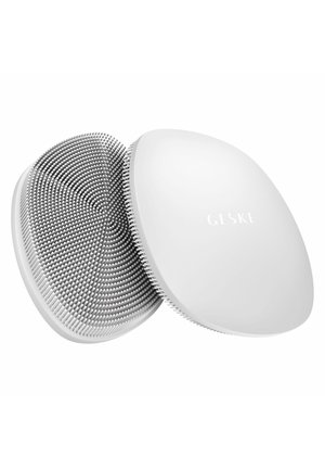 Brosse faciale circulaire en silicone blanc avec des poils doux et la marque "GESKE" sur une surface arrière lisse.