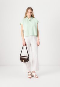 Mintgroene cropped polo shirt met korte mouwen, gecombineerd met witte broek met wijde pijpen en witte hoge hakken. Donkerbruin schoudertasje met gouden hardware.