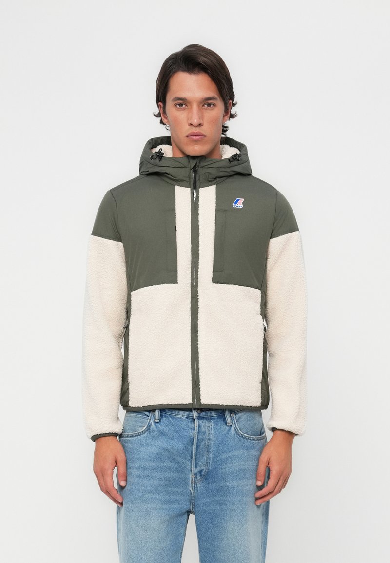 Grønn og kremfarget zip-up jakke med hette, med fleece tekstur og fargeblokkdesign. Inkluderer logo på brystet og sidelommer.