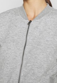 Grijze bomberjack met textuur, voorzien van een geribde kraag, ritssluiting aan de voorkant en subtiele details. Zacht stof met een casual ontwerp.