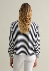 Pullover a righe in blu navy e bianco; vestibilità ampia con maniche lunghe e leggermente a sbuffo; tessuto testurizzato; orlo che cade appena sopra la vita.