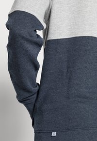 Grijze en donkerblauwe sweatshirt met lange mouwen, gestructureerde stof en een lagere zoomtag met een geometrisch logo.
