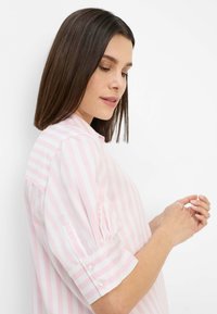 Short-sleeved, collared shirt in pink and white stripes. Features button details on sleeves, with a smooth fabric texture.
