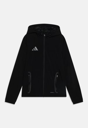 Chaqueta negra con capucha, hecha de tela suave, que presenta un cierre frontal, dos bolsillos laterales, un logo reflectante y una capucha ajustable con cordones.