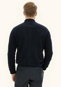 Maglione lavorato a maglia blu navy con colletto alto e maniche lunghe, caratterizzato da una texture morbida. La vista posteriore mostra una vestibilità rilassata e un design minimale.