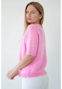 Różowy sweter z krótkim rękawem, wykonany z miękkiego, puszystego materiału. Posiada ściągacz przy dekolcie i hemie, luźny krój oraz subtelną teksturę.