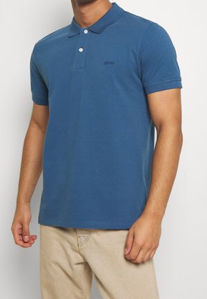 Polo en coton bleu avec col classique, deux boutons et manches courtes. Présente un logo brodé subtil sur la poitrine.