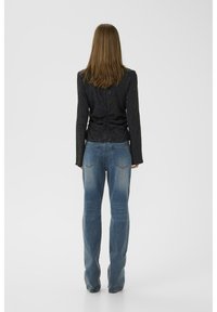 Haut à manches longues noir à motifs avec un design froncé, associé à un jean droit bleu clair. Vu de derrière.