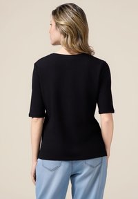 Top negro de manga corta con un escote redondo, textura suave y silueta ajustada, combinado con pantalones de un azul claro con bolsillos.