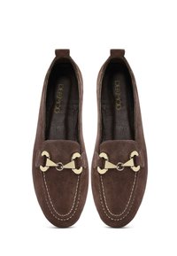 Mocassins en daim marron avec un design cousu, dotés d'un accent décoratif en métal doré à l'avant. Doublure en cuir lisse à l'intérieur.