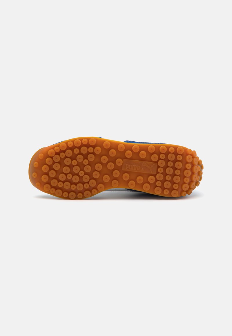 Suela de zapato Puma en goma naranja con patrones de agarre circulares y marca. La forma de la suela es curvada con una superficie texturizada para proporcionar tracción.