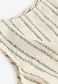Lettet beige stof med lodrette sorte striber, der har et struktureret mønster og et afslappet halsudskæring design.