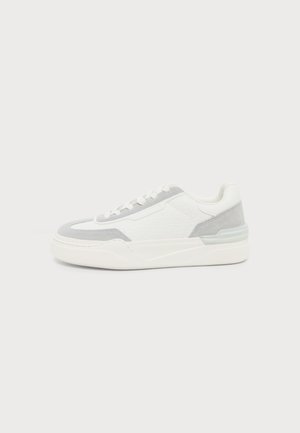 Baskets blanches avec détails en suède gris clair, panneaux latéraux texturés, lacets blancs et semelle épaisse en caoutchouc blanc, vues de côté sur fond uni.