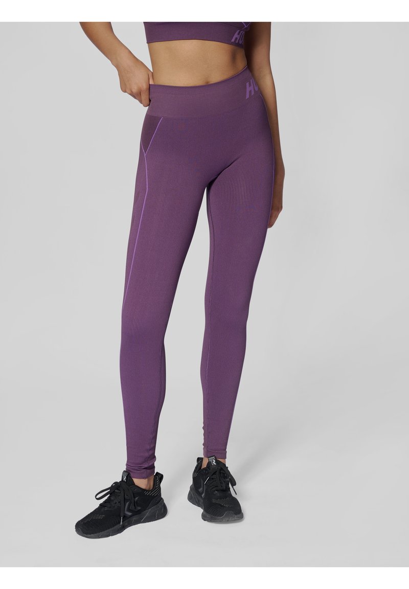 Mörklila träningsleggings med ribbat mönster, hög midja, kontrasterande lila sömmar samt en åtsittande design, i kombination med svarta sneakers.