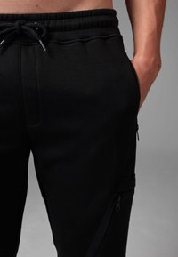 Black sweatpants with a drawstring waist, featuring side zip pockets and a smooth fabric texture. Tailored fit with minimal design details.