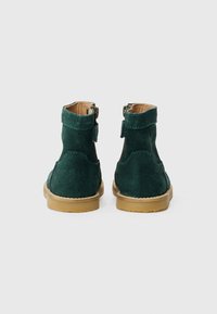 Botines de ante verde con un acabado suave, punta redonda y suela de goma marrón. Presentan un cierre lateral y costuras decorativas.