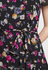 Klänning i svart tyg med flerfärgade blommönster; har en knytning i midjan och korta ärmar. Mjuk textur.