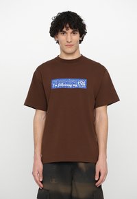 Brown cotton t-shirt with short sleeves and a crew neckline. Front graphic reads "I'M NOT LOST, I'M following my..." in blue and white text.