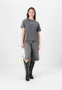 Gray, oversized t-shirt with white text; gray denim shorts; black, knee-high cowboy boots with white embroidery; white handbag.