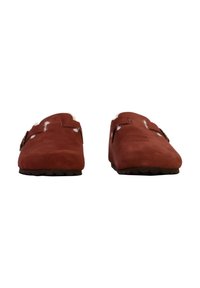 Zoccoli rossi in suede con suola piatta, caratterizzati da doppi dettagli con fibbie sulla tomaia e un morbido rivestimento bianco. Superficie testurizzata per una migliore aderenza.