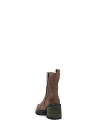 Bottine en cuir suédé marron avec fermeture éclair, talon épais vert et semelle texturée noire, mettant en avant un design élégant et une forme structurée.