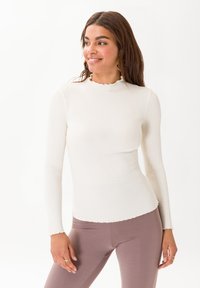 Maglietta a maniche lunghe a coste bianca con scollatura e orlo scallop. Abbinata a leggings marrone chiaro, presenta una silhouette aderente.