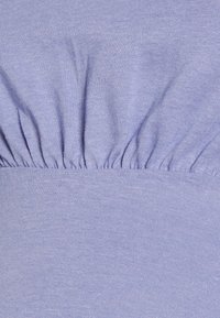 Tecido roxo claro com uma textura franzida na parte superior, parte inferior lisa e cintura elástica. Material macio e elástico.