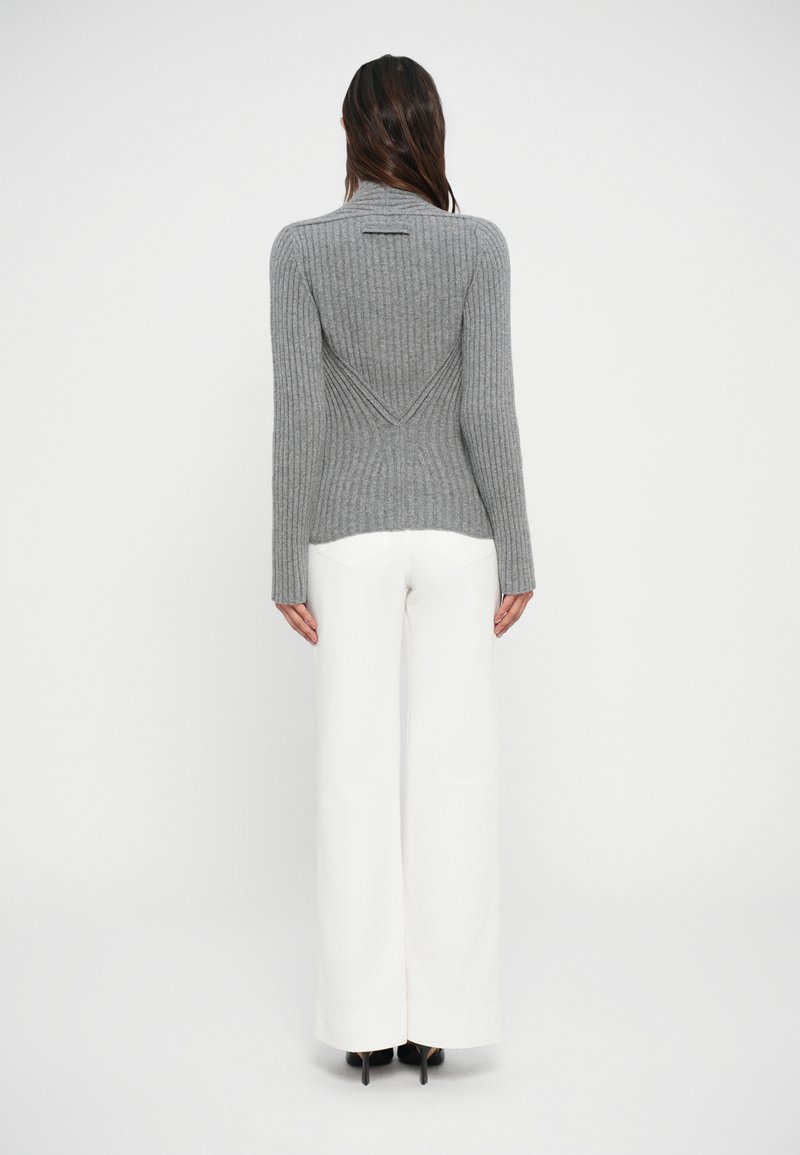 Gray ribbed sweater with a high collar, featuring a diagonal back seam. Paired with white wide-leg trousers and black high heels.