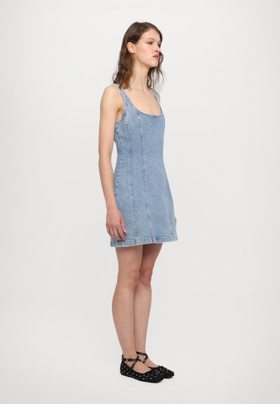 Denimkleit õhuke rihmadega, millel on tihe kevadosa, laienev allosa ja nähtavad õmblused. Kantud mustade täpikatega tasaste jalanõudega.