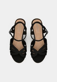 Sandales noires à bout ouvert, brides texturées avec motifs découpés, bride de cheville ajustable et première de propreté rembourrée de couleur marron clair.