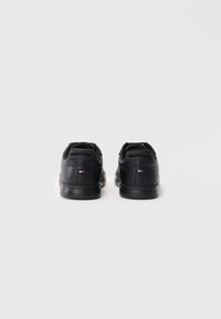 Czarne skórzane sneakersy z gładką teksturą, wyściełanym kołnierzem i małym logo na pięcie. Płaska gumowa podeszwa dla komfortu.