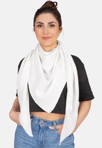 Écharpe texturée blanche drapée en forme de triangle, avec deux longues extrémités laissant pendre. Portée sur un top noir court.