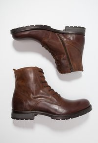Bottines en cuir marron avec des fermetures à lacets et à glissière, surfaces texturées et semelles robustes avec un motif de griffage.