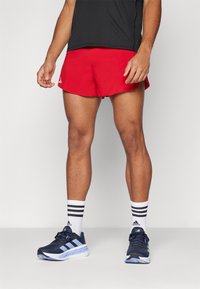 Rote Sportshorts mit einem elastischen Bund, kombiniert mit marineblauen Laufschuhen mit hellblauen Akzenten und schwarz-weißen gestreiften Socken.