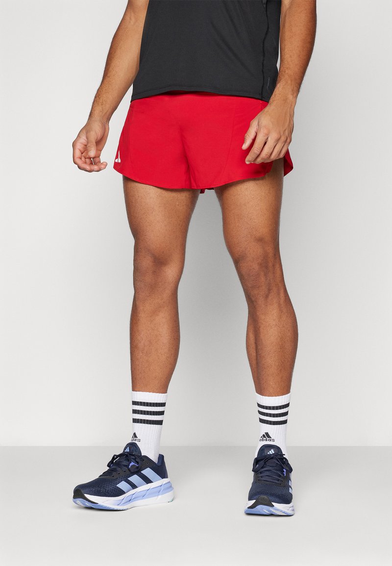 Rote Sportshorts mit einem elastischen Bund, kombiniert mit marineblauen Laufschuhen mit hellblauen Akzenten und schwarz-weißen gestreiften Socken.