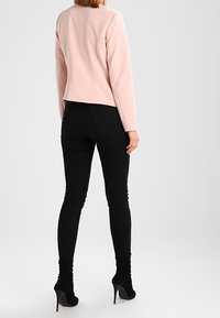 Veste rose pâle texturée à manches longues, avec un col rond, associée à un jean skinny noir et des bottines.